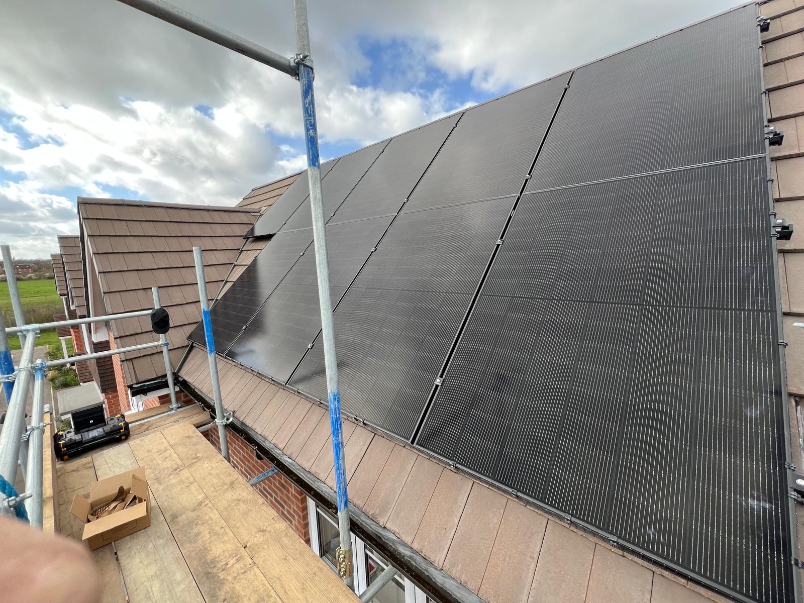 Solar panels installed on a pitched roof with scaffolding along the roofline, photographed by Cozy Home Solutions during a live installation.